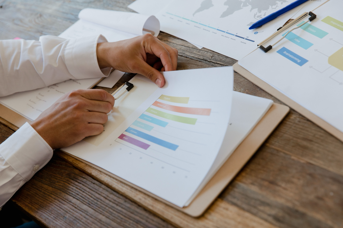 Hands reviewing colorful analytics bar charts on a clipboard beside a strategy planning board