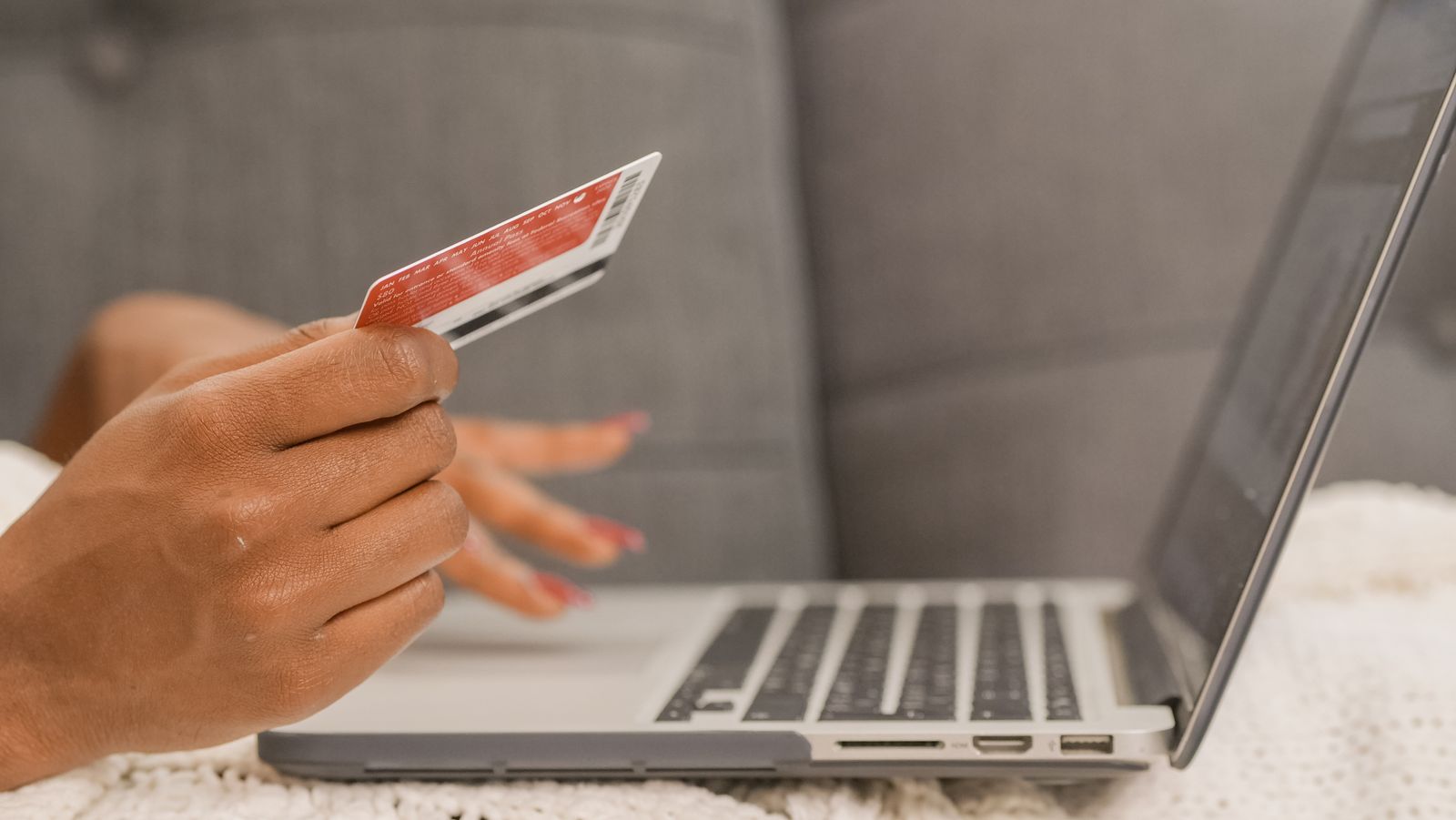Hand holding a credit card next to a laptop during online checkout